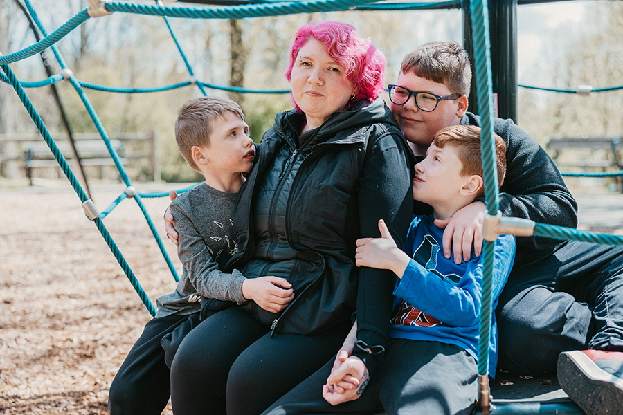 mom and three sons sitting on playground equipment, hugging